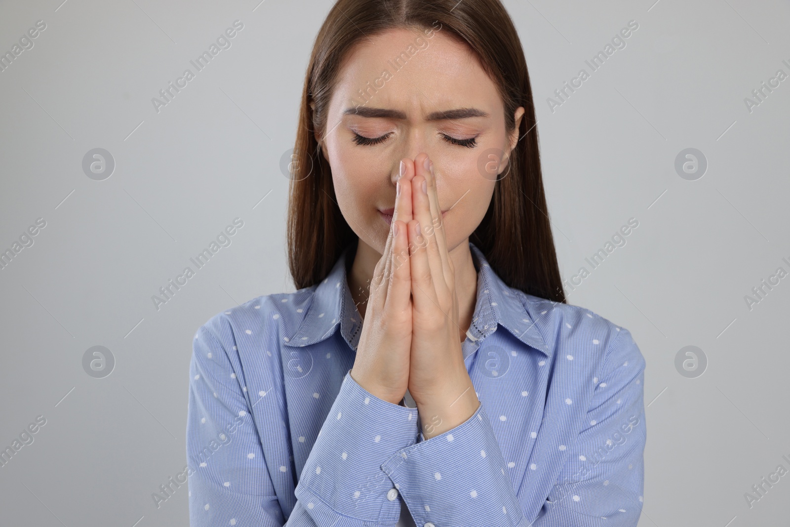 Photo of Woman with clasped hands praying on light grey background