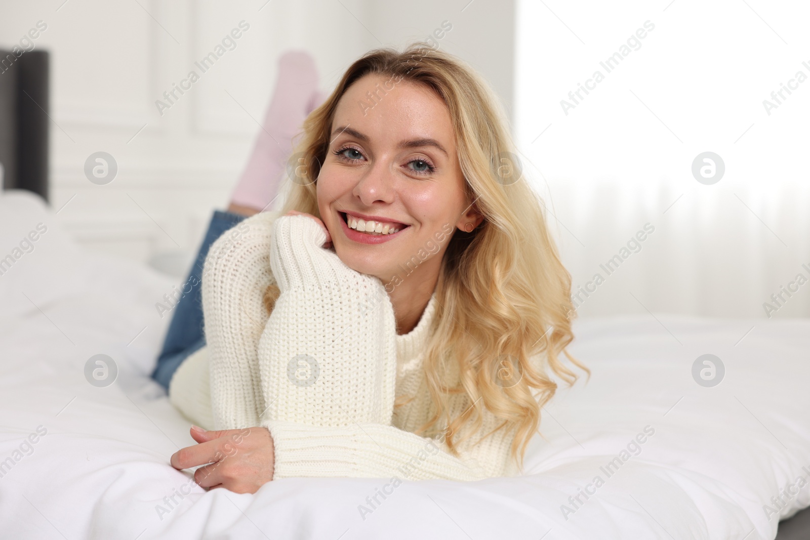 Photo of Happy woman in stylish warm sweater lying on bed indoors