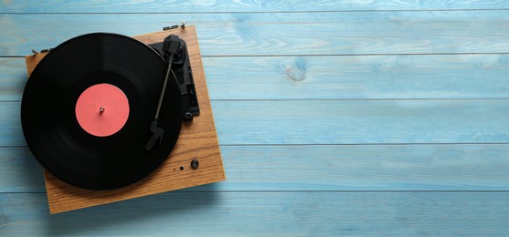 Photo of Turntable with vinyl record on light blue wooden background, top view. Space for text