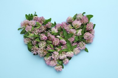 Heart made of beautiful clover flowers with green leaves on light blue background, flat lay