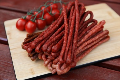 Photo of Tasty dry cured sausages (kabanosy) and tomatoes on wooden table, closeup