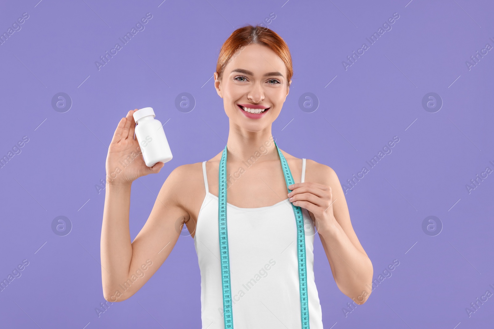 Photo of Happy young woman with bottle of pills and measuring tape on purple background. Weight loss