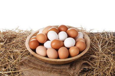 Fresh chicken eggs in bowl and dried straw on table against white background