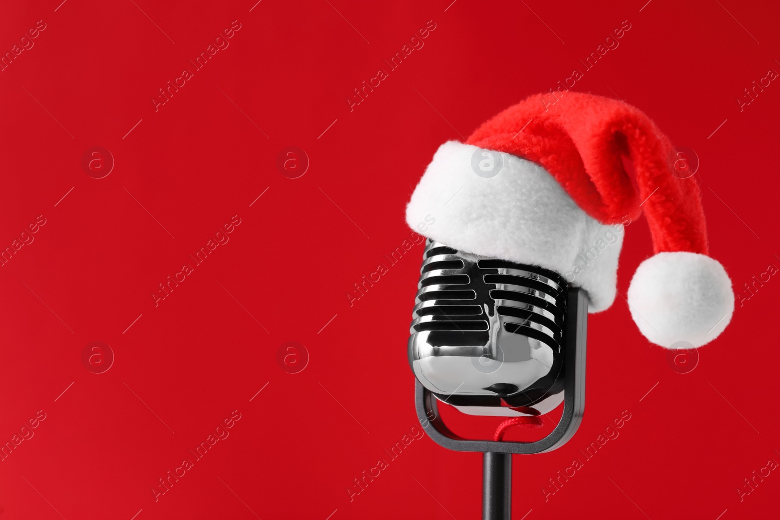 Photo of Retro microphone with Santa hat on red background, space for text. Christmas music
