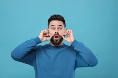 Surprised young man touching mustache on light blue background