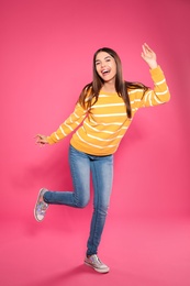 Full length portrait of emotional woman dancing on color background