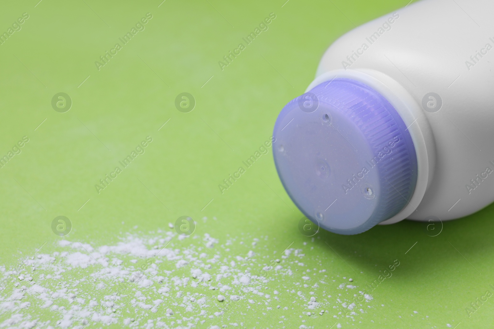 Photo of Bottle and scattered dusting powder on light green background, space for text. Baby cosmetic product