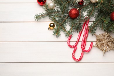 Flat lay composition with tasty candy canes and Christmas decor on white wooden table, space for text