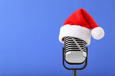 Photo of Retro microphone with Santa hat on blue background, space for text. Christmas music