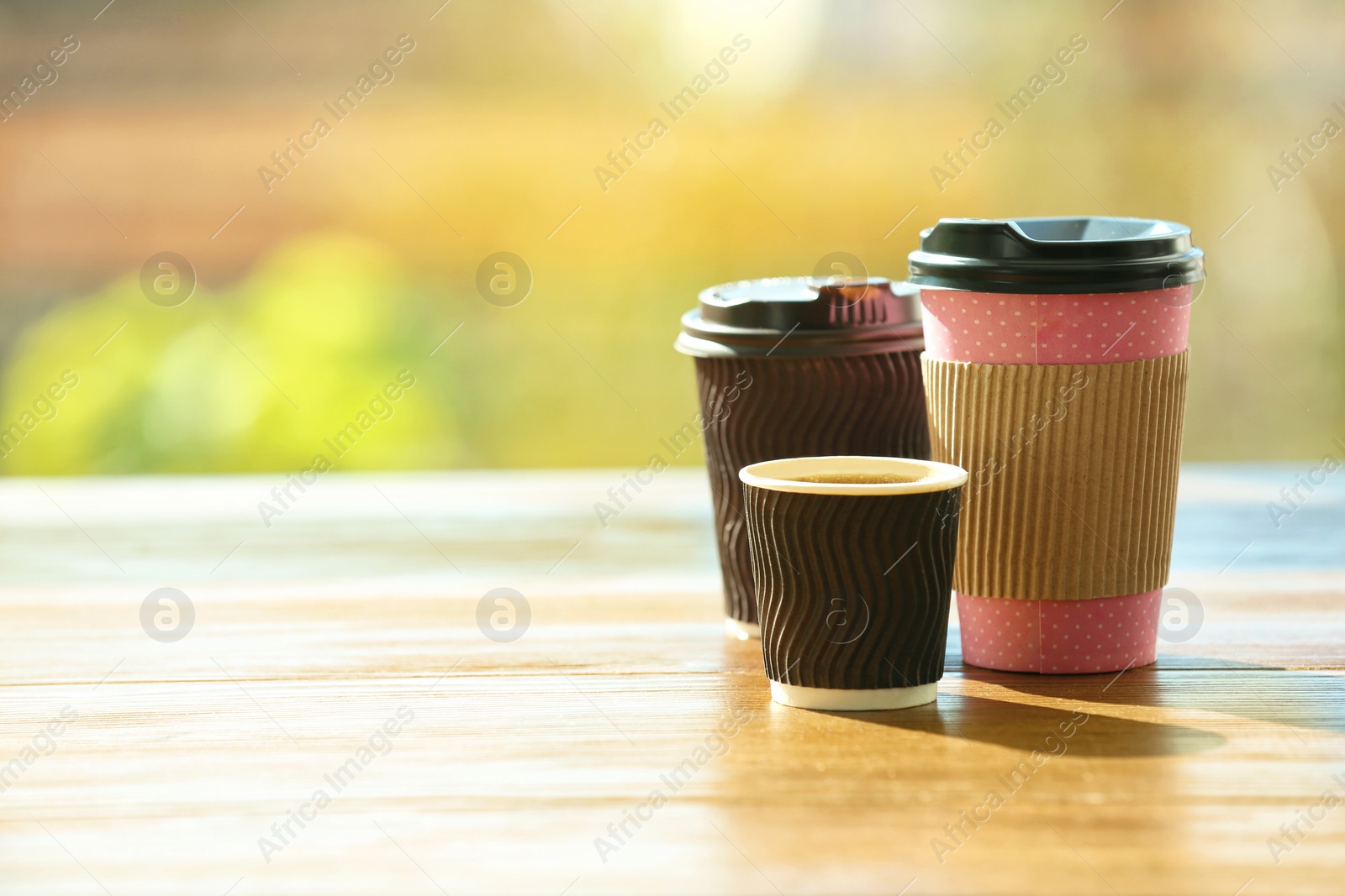 Photo of Cardboard cups of coffee on table against blurred background. Space for text
