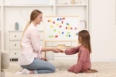 Photo of Mom teaching her daughter alphabet with magnetic letters at home