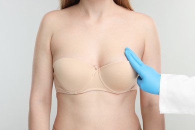 Mammologist checking woman's breast on light grey background, closeup