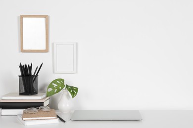 Cozy workspace with laptop, houseplant and stationery on white desk at home