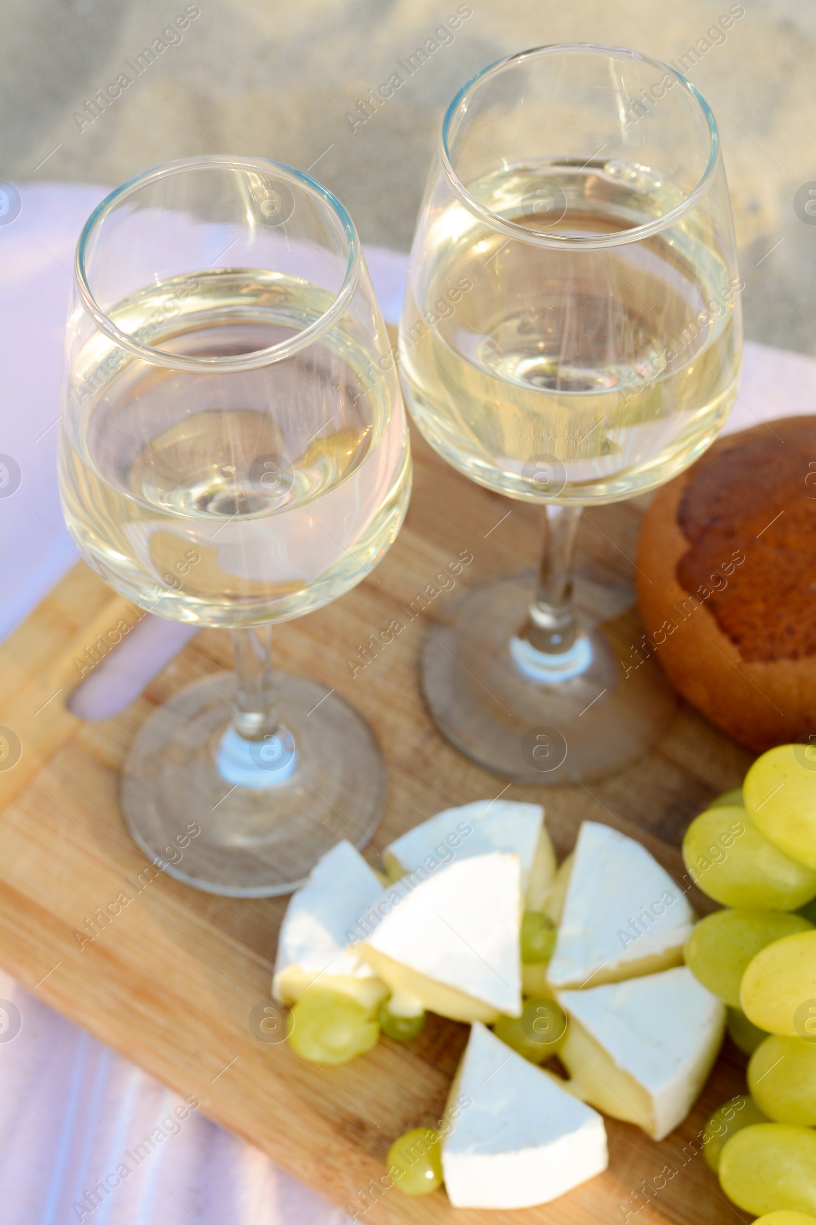 Photo of Glasses with white wine and snacks for beach picnic on sand outdoors