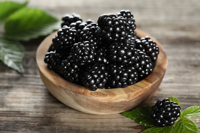 Ripe blackberries and green leaves on wooden table, closeup