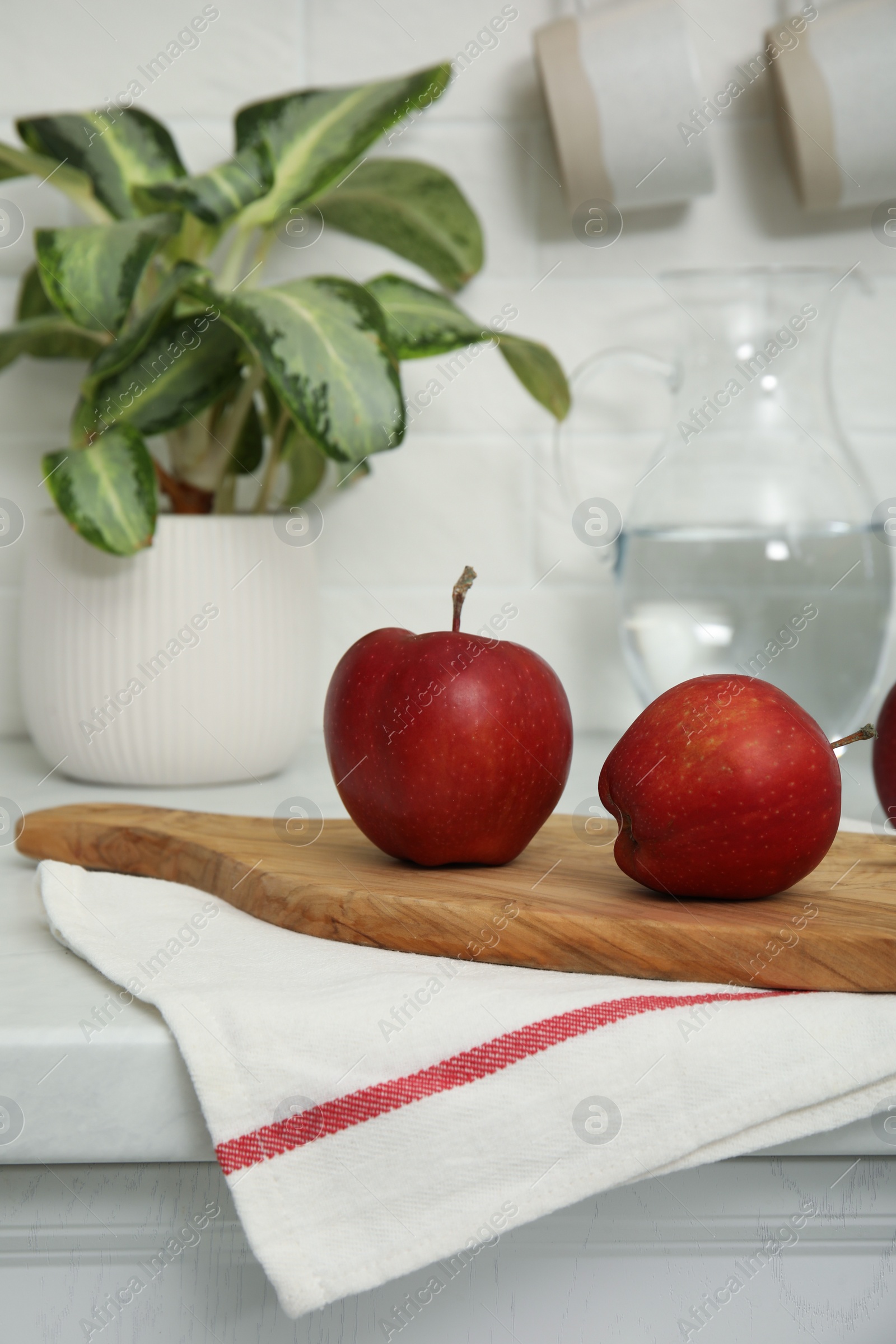 Photo of Clean towel and wooden board with ripe apples on countertop in kitchen