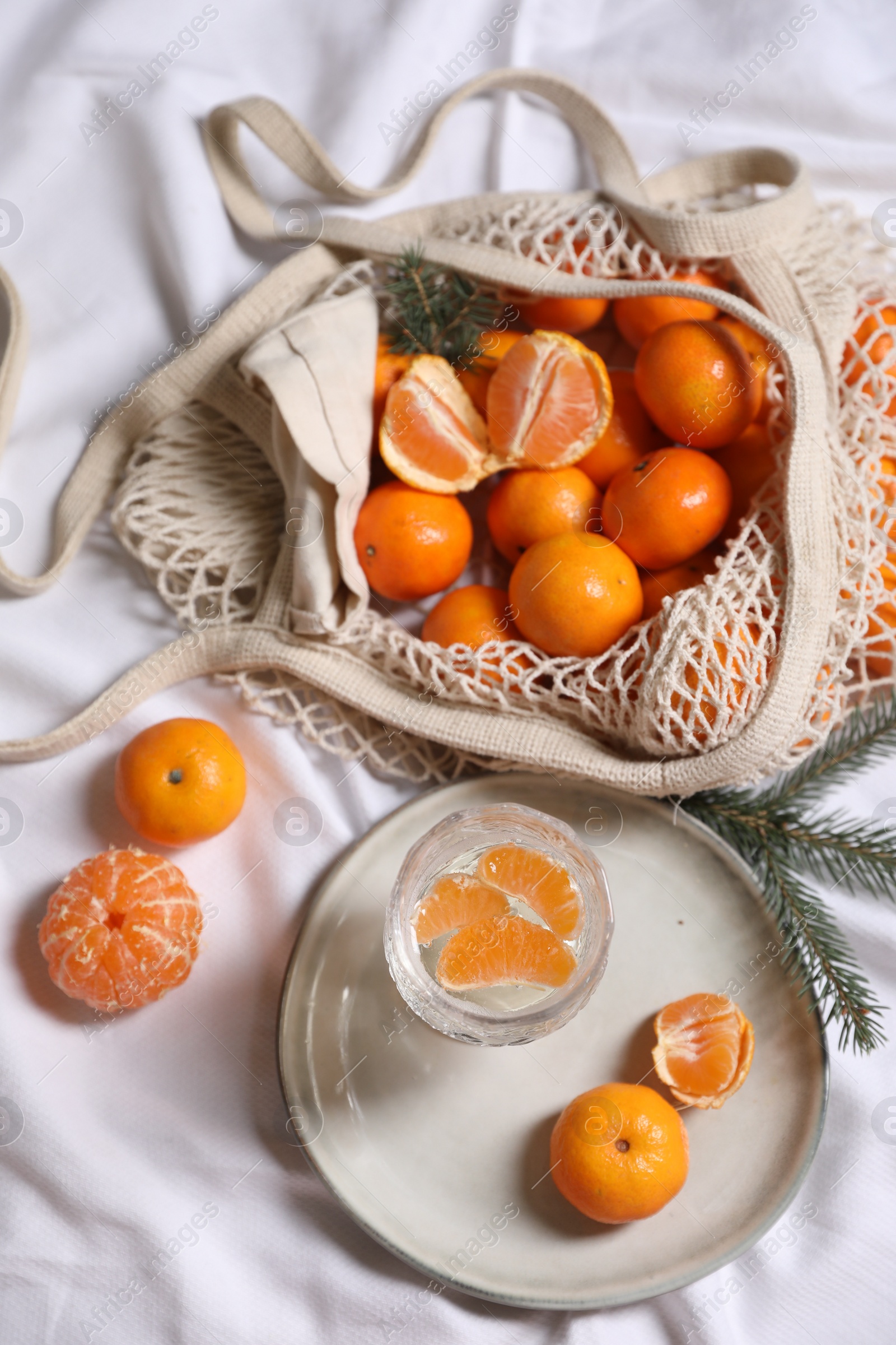 Photo of Delicious ripe tangerines, glass with sparkling wine and fir branch on white bedsheet, flat lay