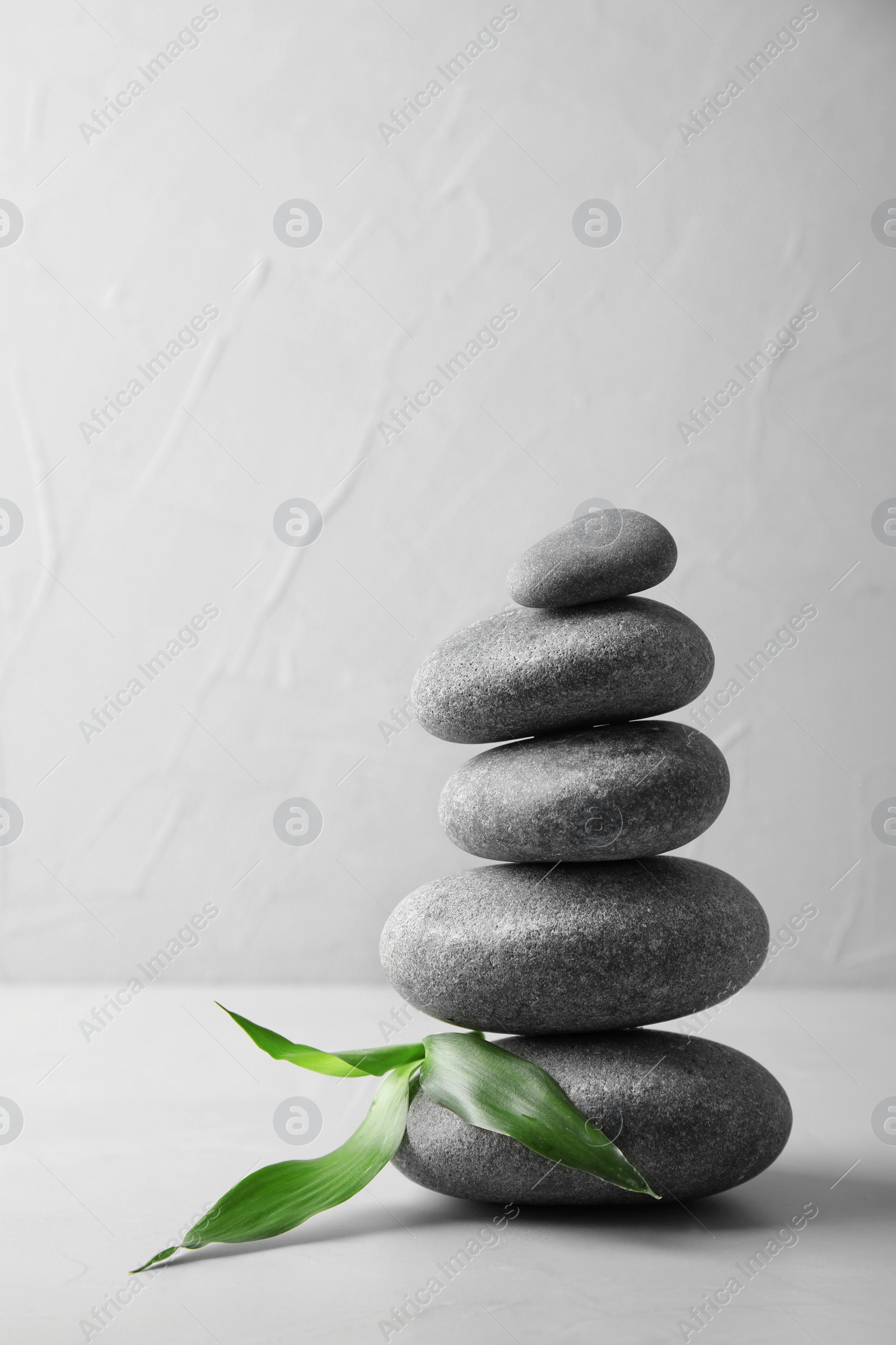 Photo of Stack of zen stones and bamboo leaves on table against light background. Space for text