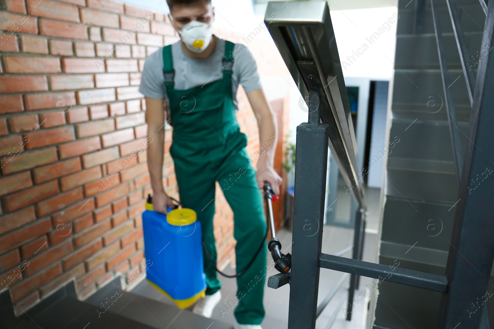 Photo of Pest control worker spraying pesticide on stairs indoors