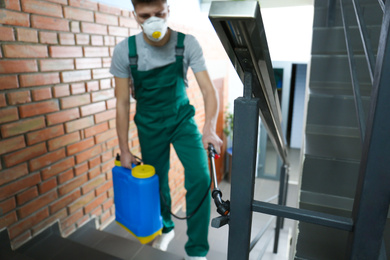 Photo of Pest control worker spraying pesticide on stairs indoors