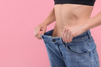 Photo of Slim woman wearing big jeans on pink background, closeup and space for text. Weight loss