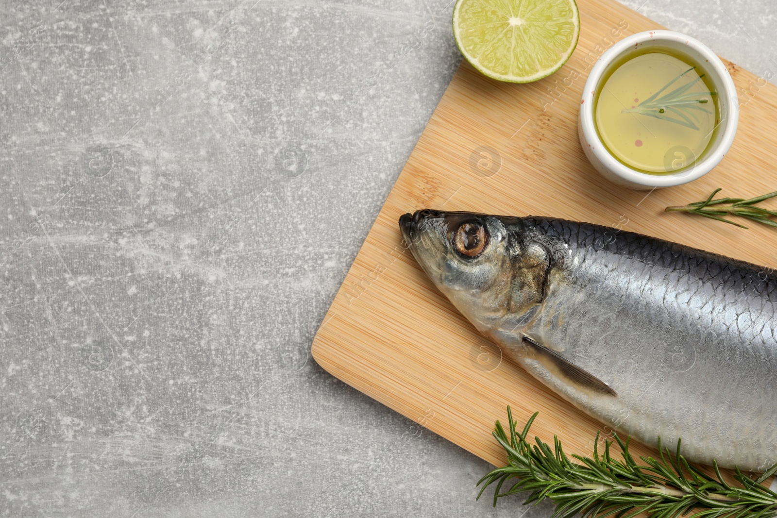 Photo of Wooden board with salted herring, lime, oil and rosemary on grey table, top view. Space for text