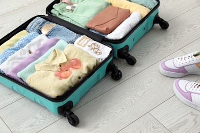 Photo of Open suitcase packed for trip and shoes on floor