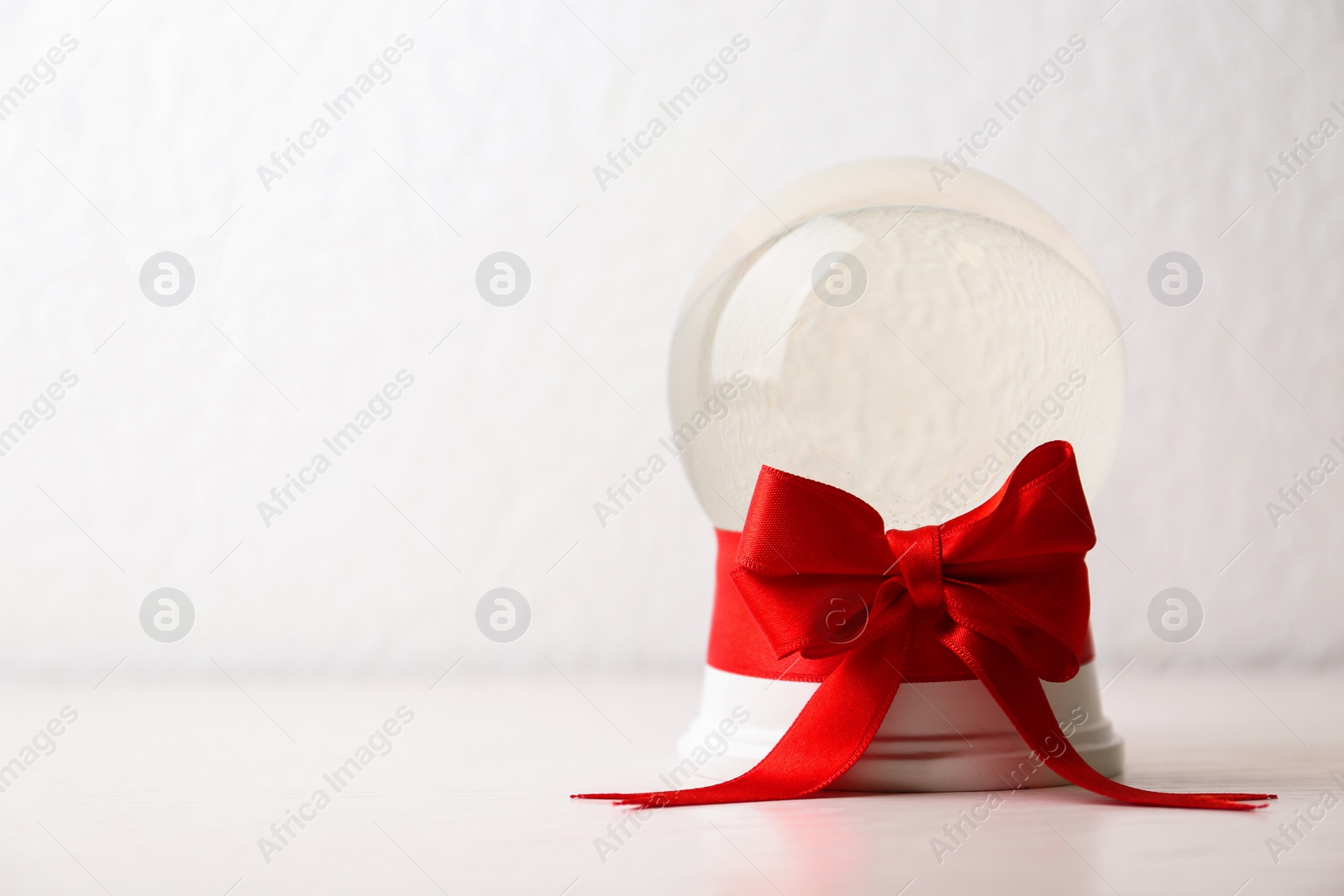 Photo of Beautiful Christmas snow globe with red bow on table against light background, space for text