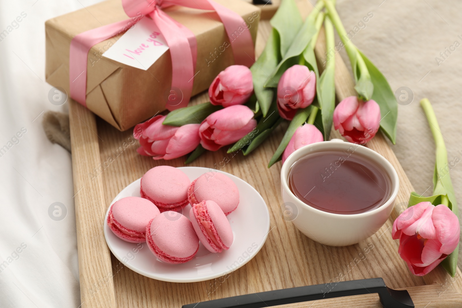 Photo of Tasty breakfast served in bed. Delicious macarons, tea, flowers, gift box and card with phrase I Love You on tray