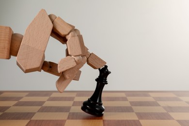 Photo of Robot touching chess piece on board against light background. Wooden hand representing artificial intelligence