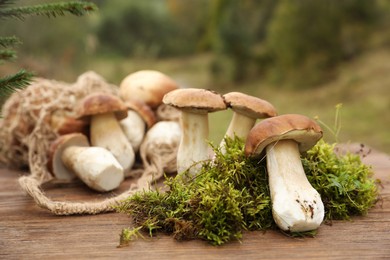 Photo of String bag and fresh wild mushrooms on wooden table outdoors