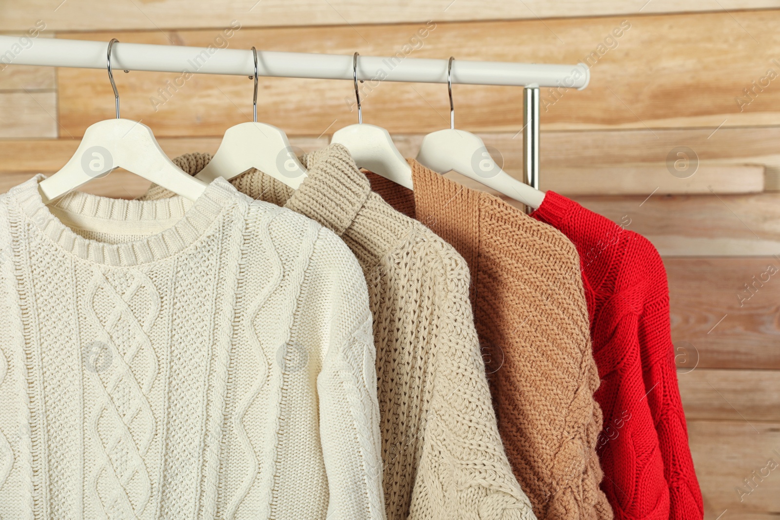 Photo of Collection of warm sweaters hanging on rack against wooden background