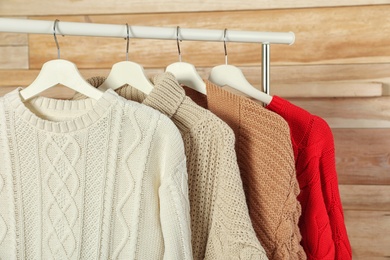 Collection of warm sweaters hanging on rack against wooden background