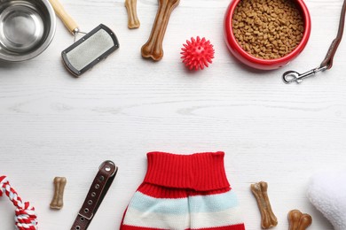 Photo of Flat lay composition with dog clothes, food and accessories on white wooden table. Space for text