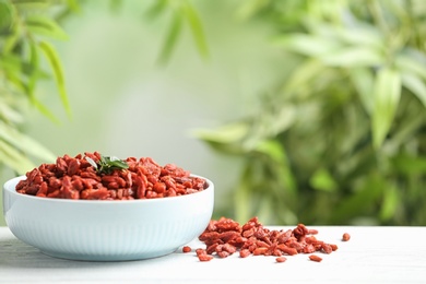 Photo of Bowl of dried goji berries on table against blurred background. Space for text