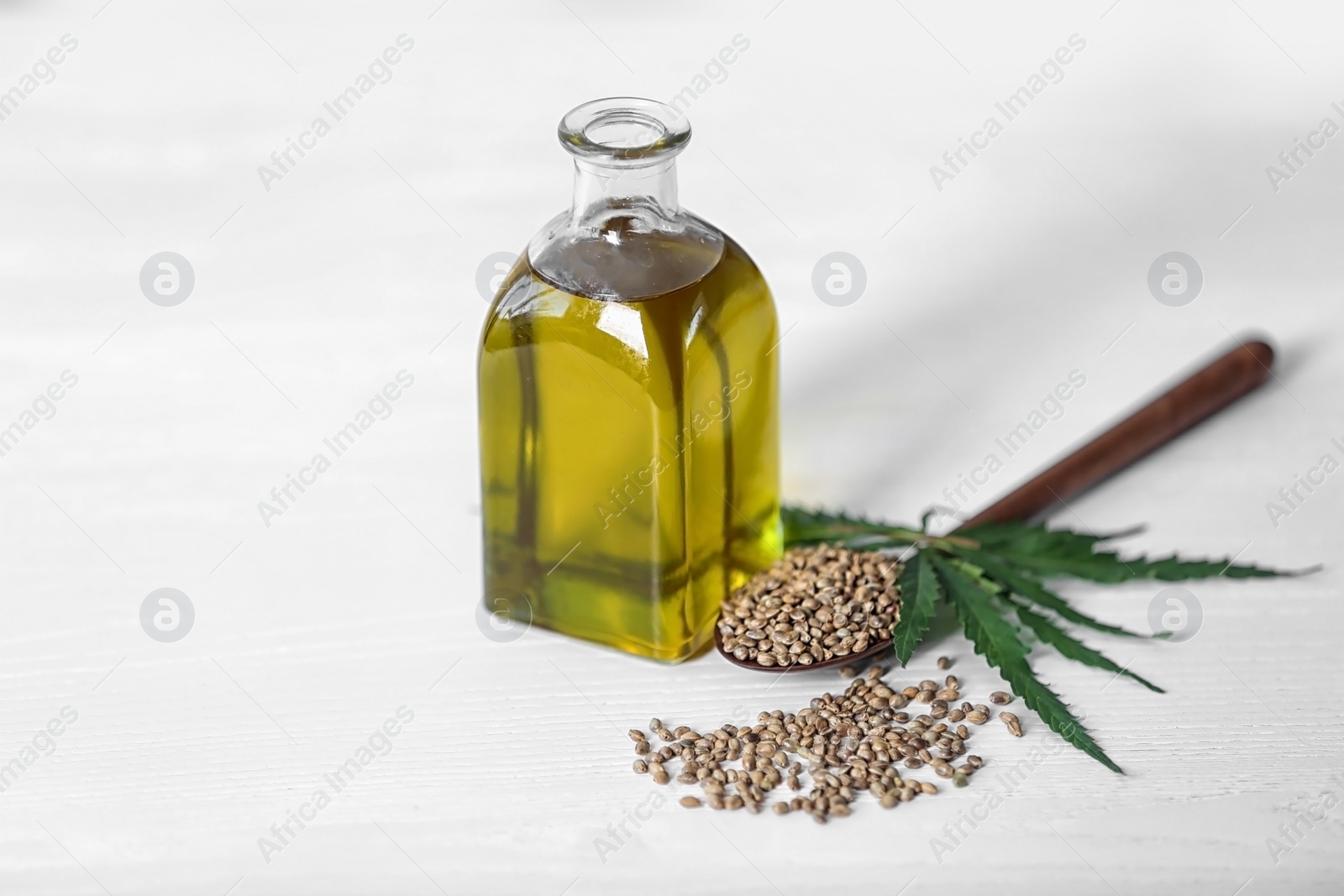 Photo of Bottle with hemp oil, seeds and fresh leaves on light table