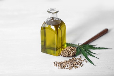 Bottle with hemp oil, seeds and fresh leaves on light table