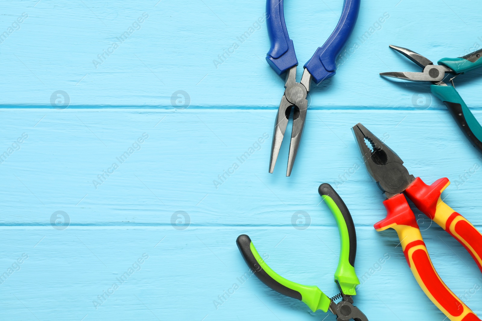 Photo of Different pliers on light blue wooden table, flat lay. Space for text