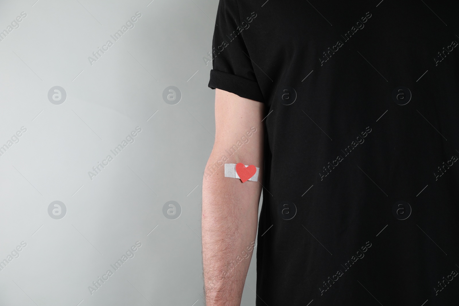 Photo of Blood donation concept. Man with adhesive plaster on arm against grey background, closeup. Space for text