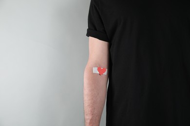 Photo of Blood donation concept. Man with adhesive plaster on arm against grey background, closeup. Space for text