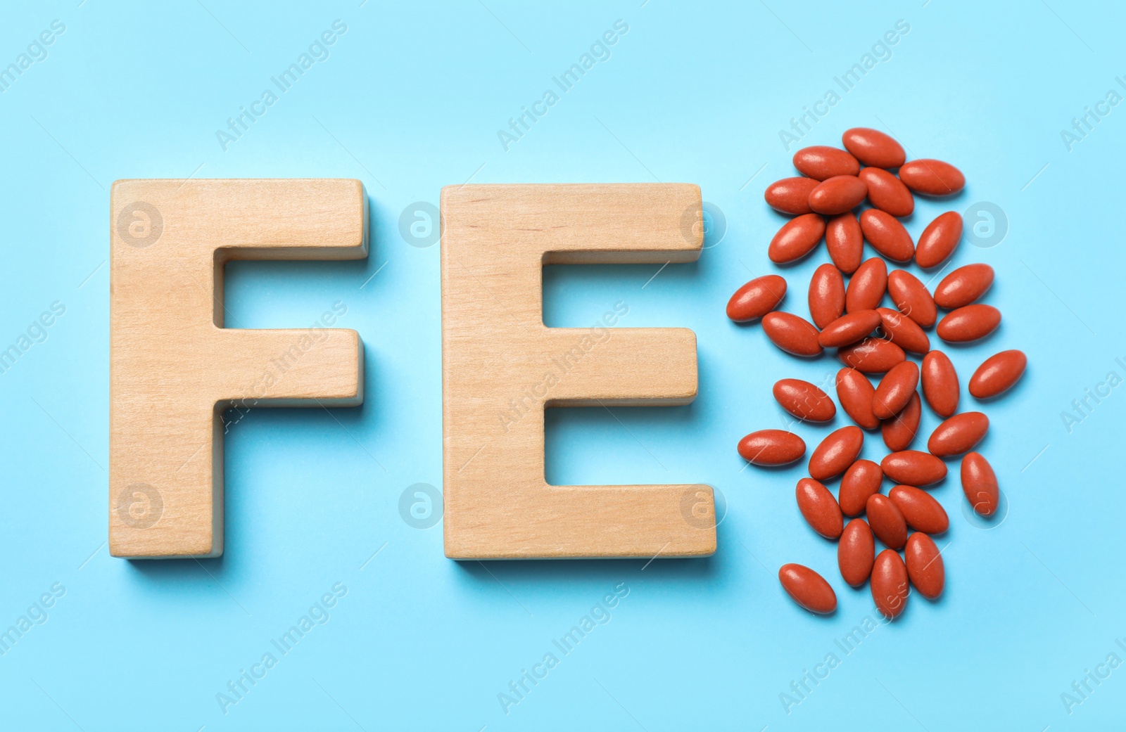 Photo of Wooden letters FE and pills on light blue background, flat lay. Anemia treatment