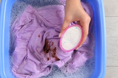 Photo of Woman adding powdered detergent into basin with clothes, top view. Hand washing laundry