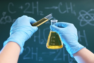Scientist pouring liquid into flask against chalkboard, closeup. Chemistry glassware