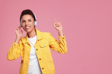 Photo of Happy young woman in headphones dancing on pink background. Space for text