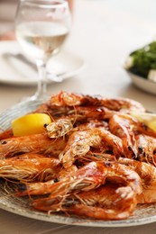 Photo of Plate of delicious cooked shrimps served with lemon and wine at table, closeup