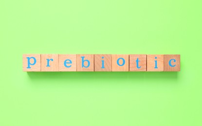 Photo of Word Prebiotic made of cubes with letters on light green background, top view