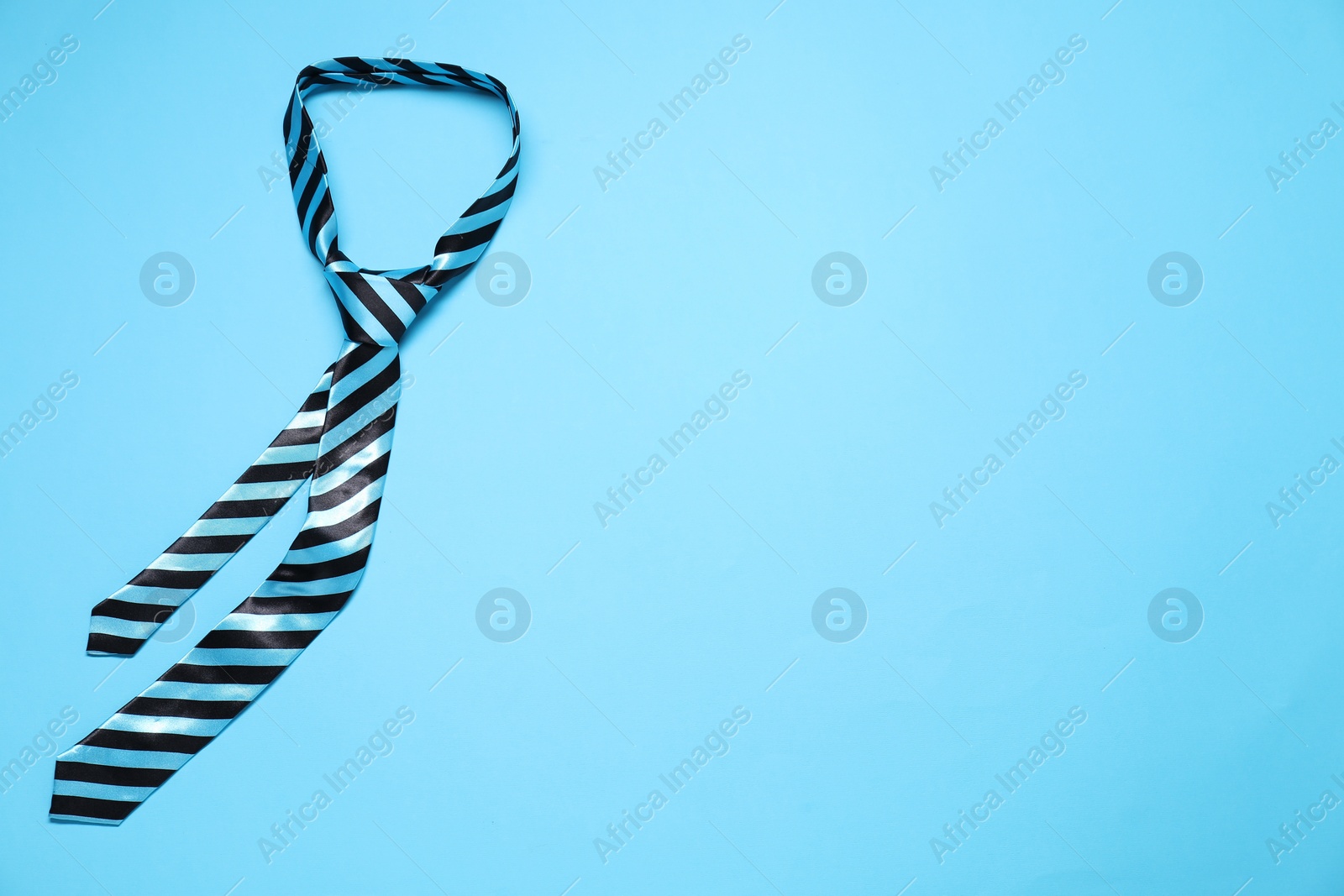 Photo of Striped necktie on light blue background, top view. Space for text