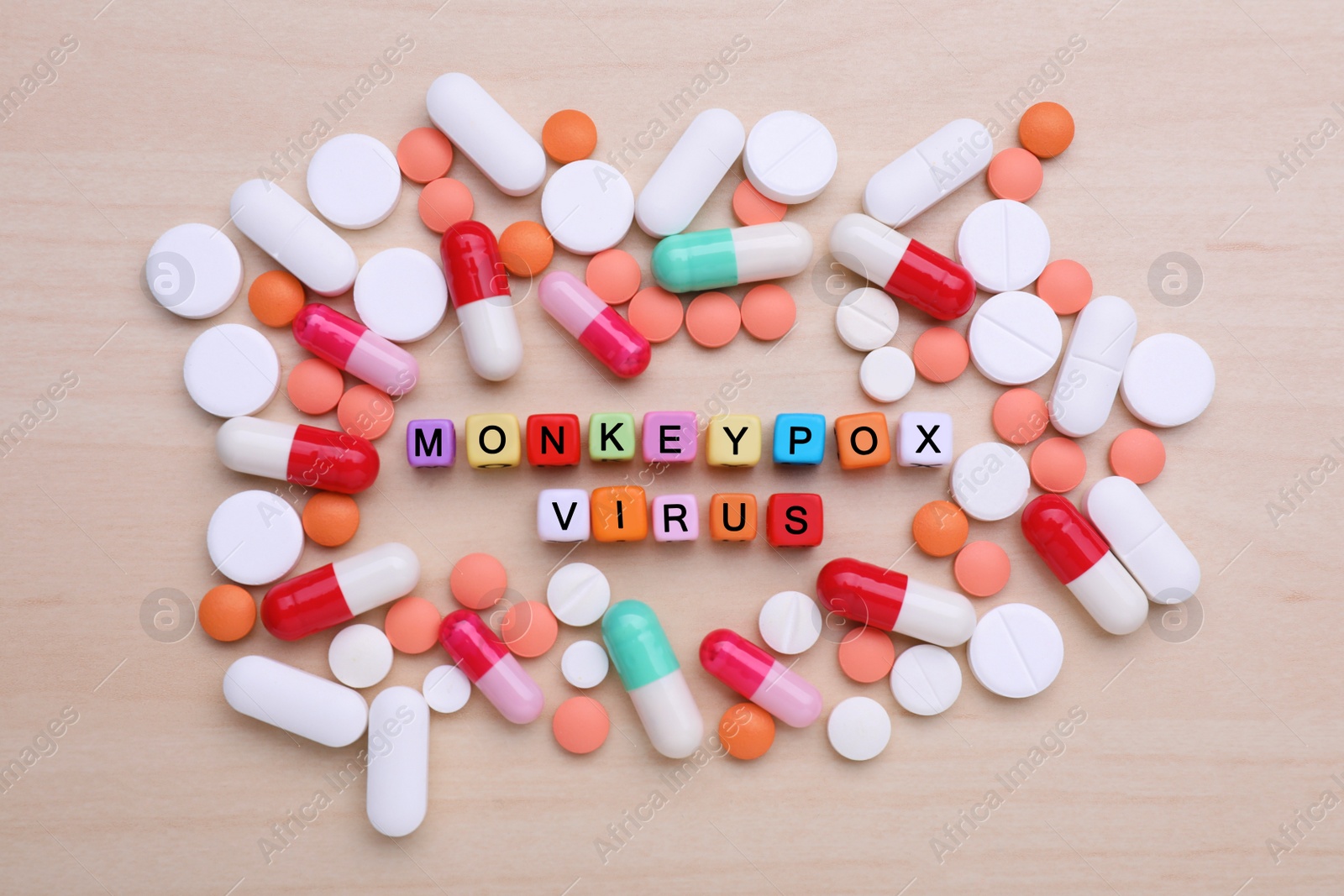 Photo of Words Monkeypox Virus made of colorful cubes surrounded by different pills on wooden table, flat lay