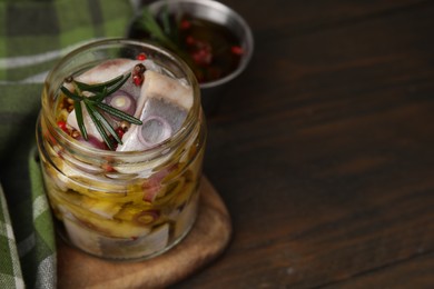 Tasty marinated fish with onion and rosemary in jar on wooden table, closeup. Space for text