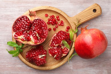 Photo of Fresh pomegranates and green leaves on wooden table, top view